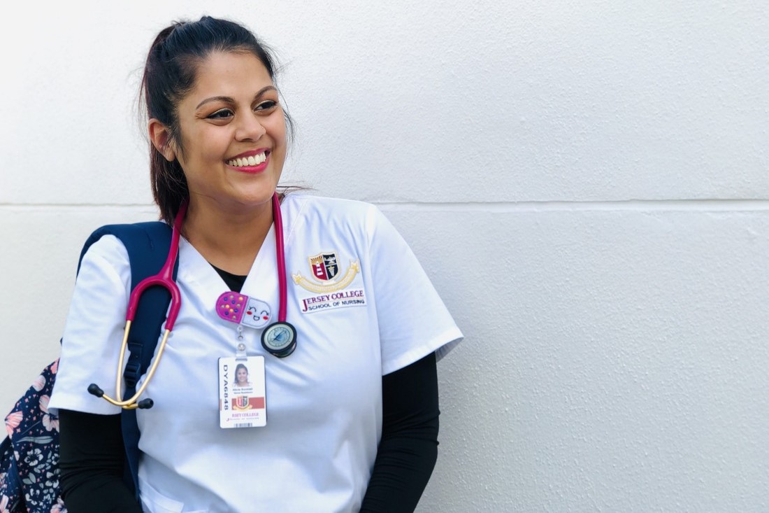 A Jersey College student poses in her nursing uniform with a hospital badge, stethoscope, and backpack. 